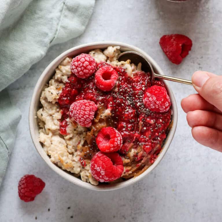 Peanut Butter and Raspberry Chia Jam Vegan Oatmeal close up in a bowl with a gold spoon. 