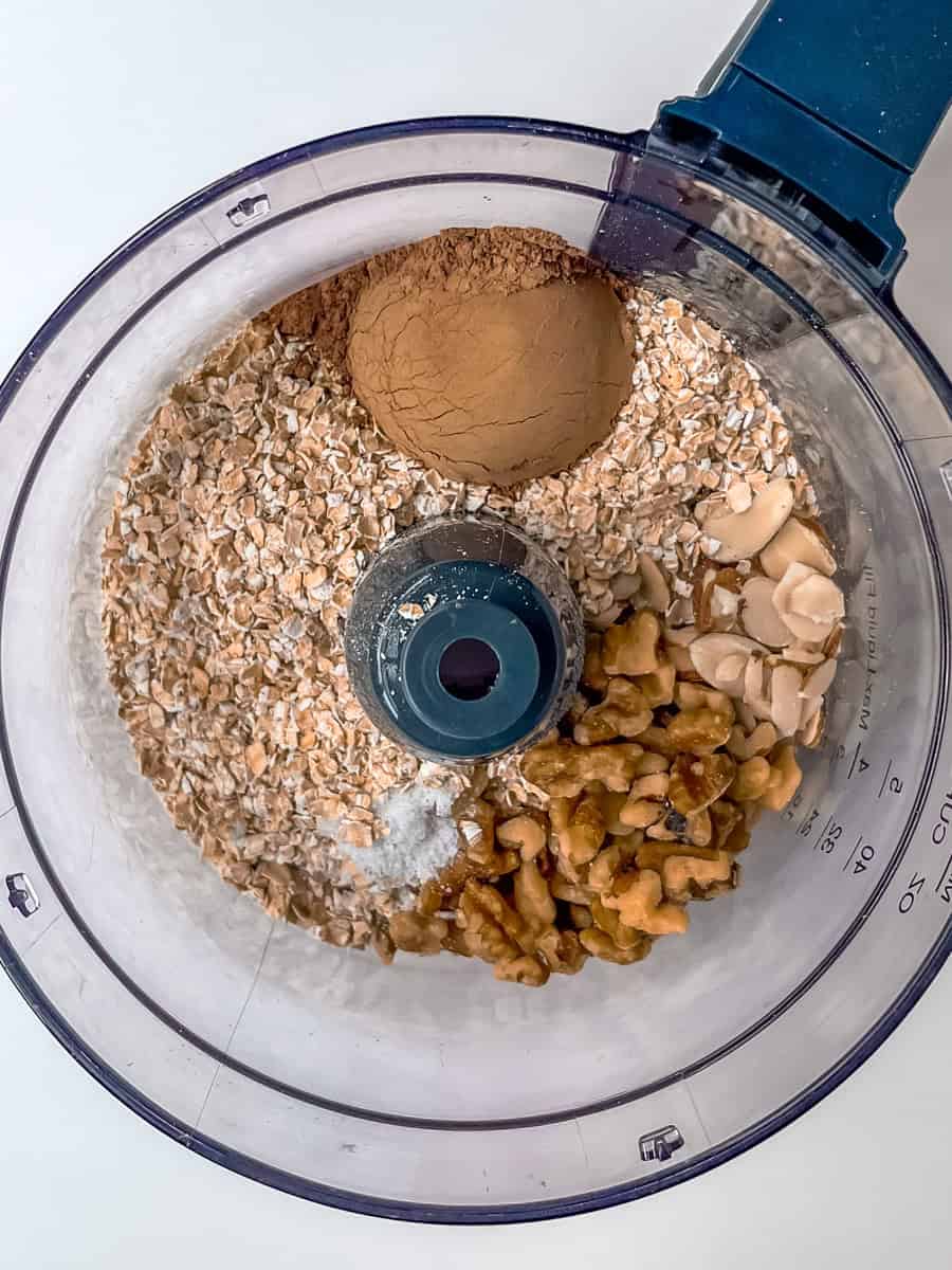 Dry ingredients (oats, walnuts, almonds, cacoa, salt) in the bowl of a food processor. 